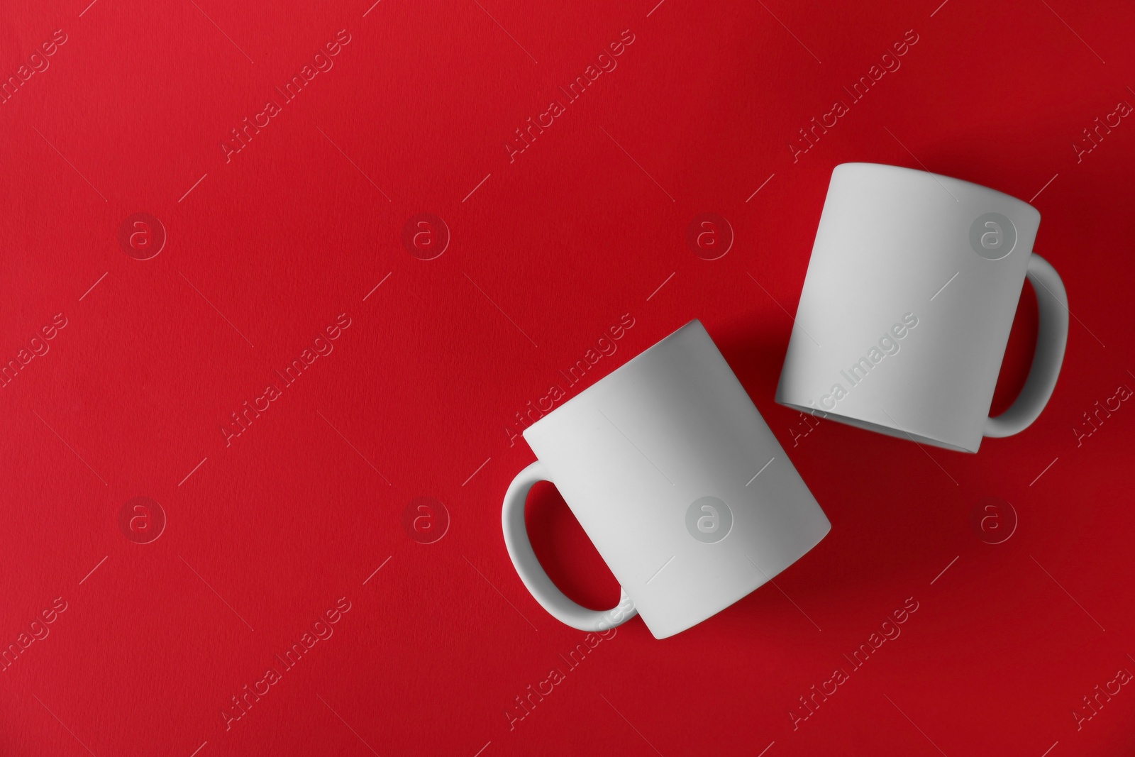 Photo of Two blank white mugs on red background, top view. Mockup for design