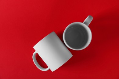 Photo of Two blank white mugs on red background, top view. Mockup for design