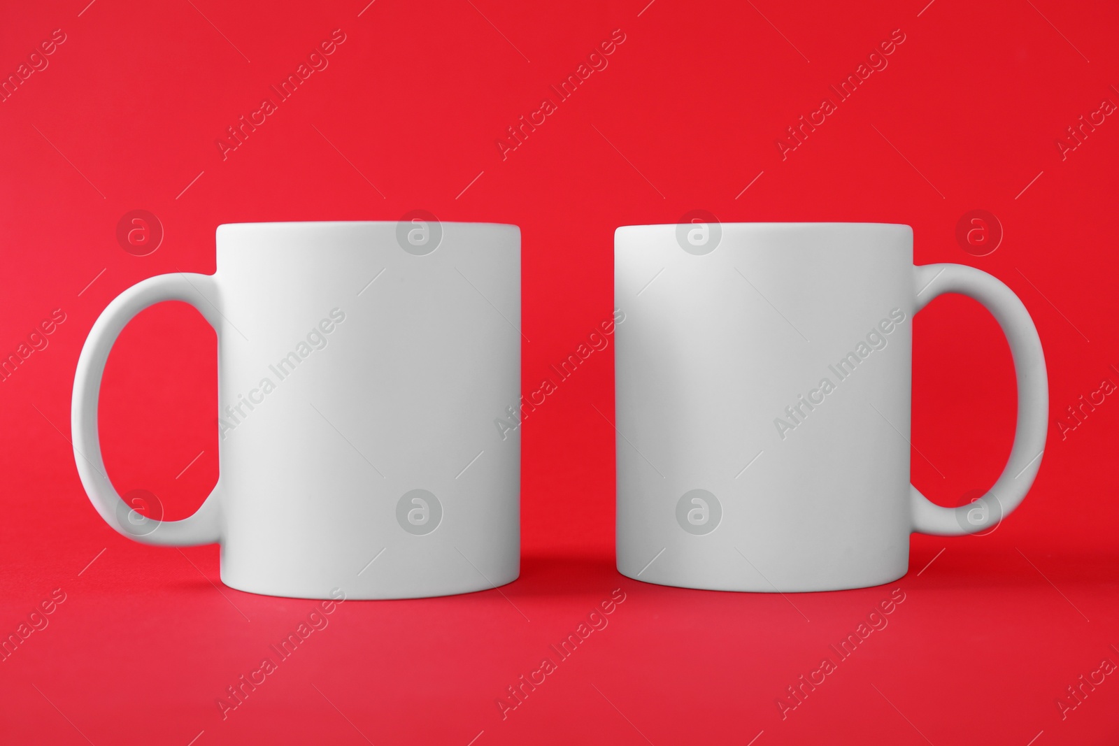 Photo of Two blank white mugs on red background. Mockup for design