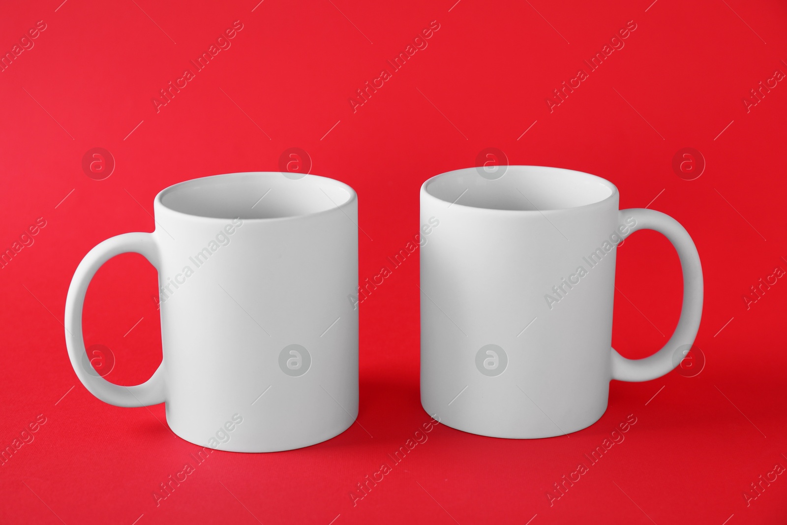 Photo of Two blank white mugs on red background. Mockup for design