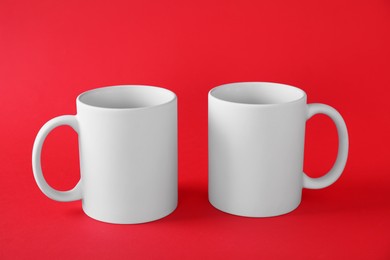 Photo of Two blank white mugs on red background. Mockup for design