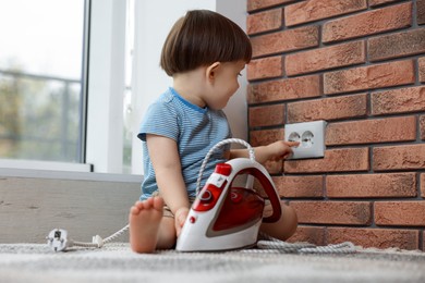 Photo of Little boy playing with electrical socket and iron at home. Child in danger