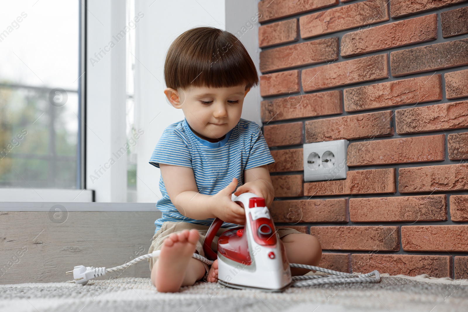 Photo of Little boy playing with iron at home. Child in danger