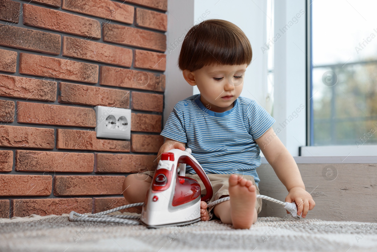 Photo of Little boy playing with iron plug near electrical socket at home. Child in danger