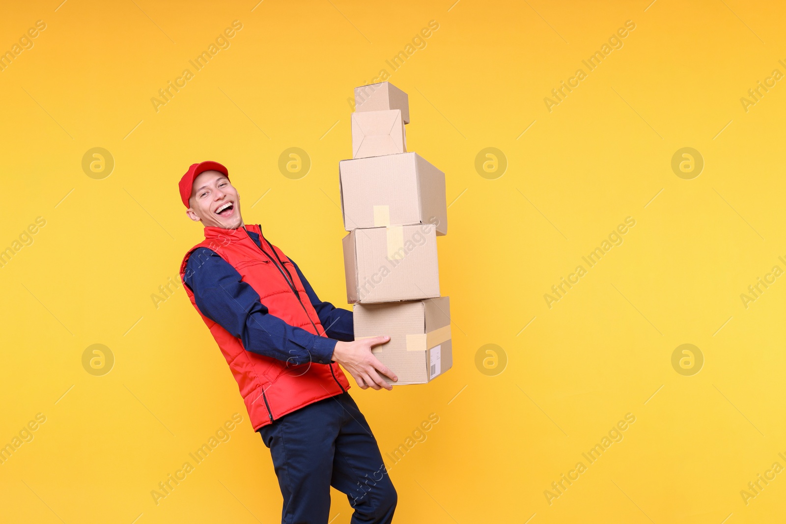 Photo of Happy postman with parcels on yellow background. Space for text