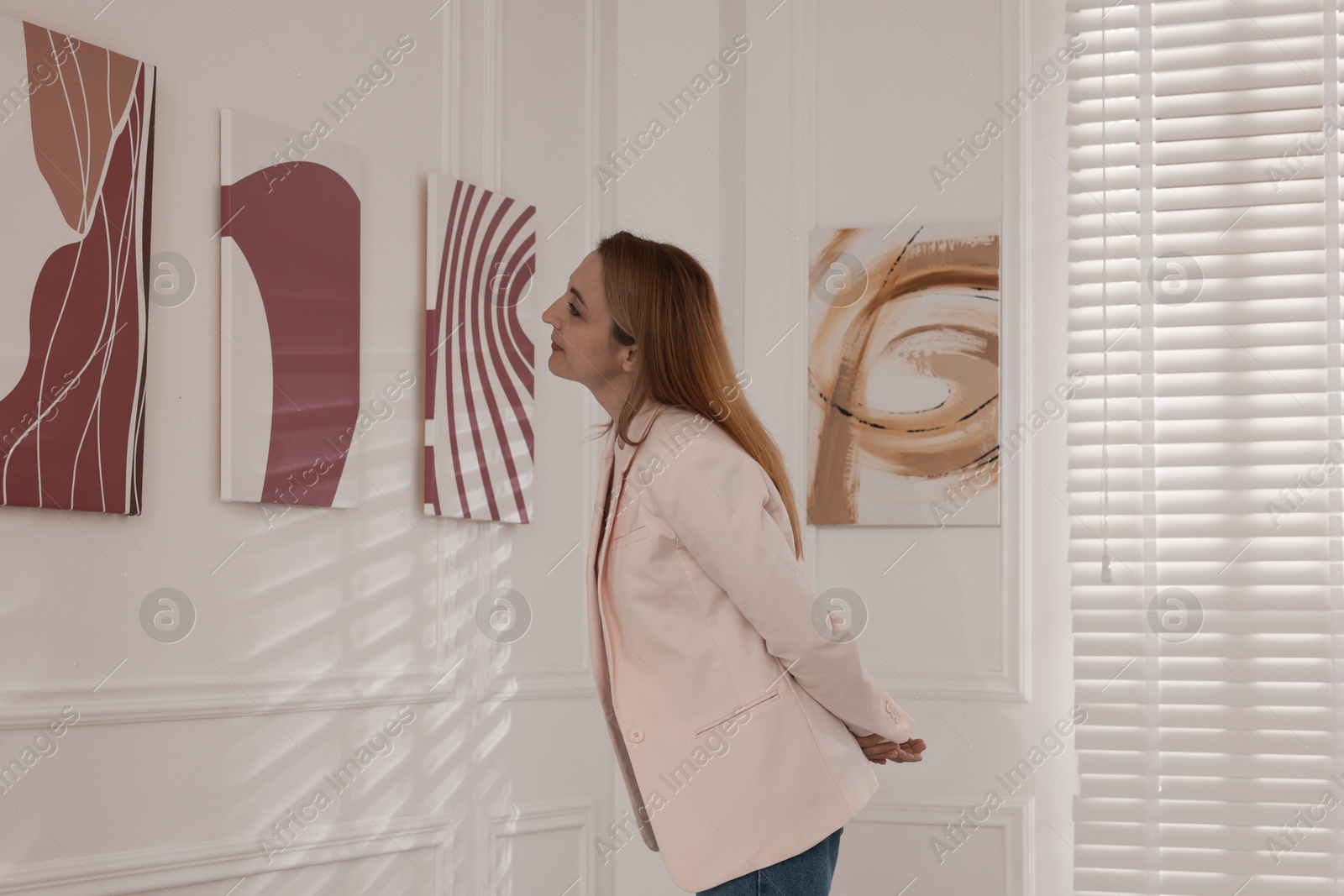 Photo of Woman examining beautiful paintings in art gallery