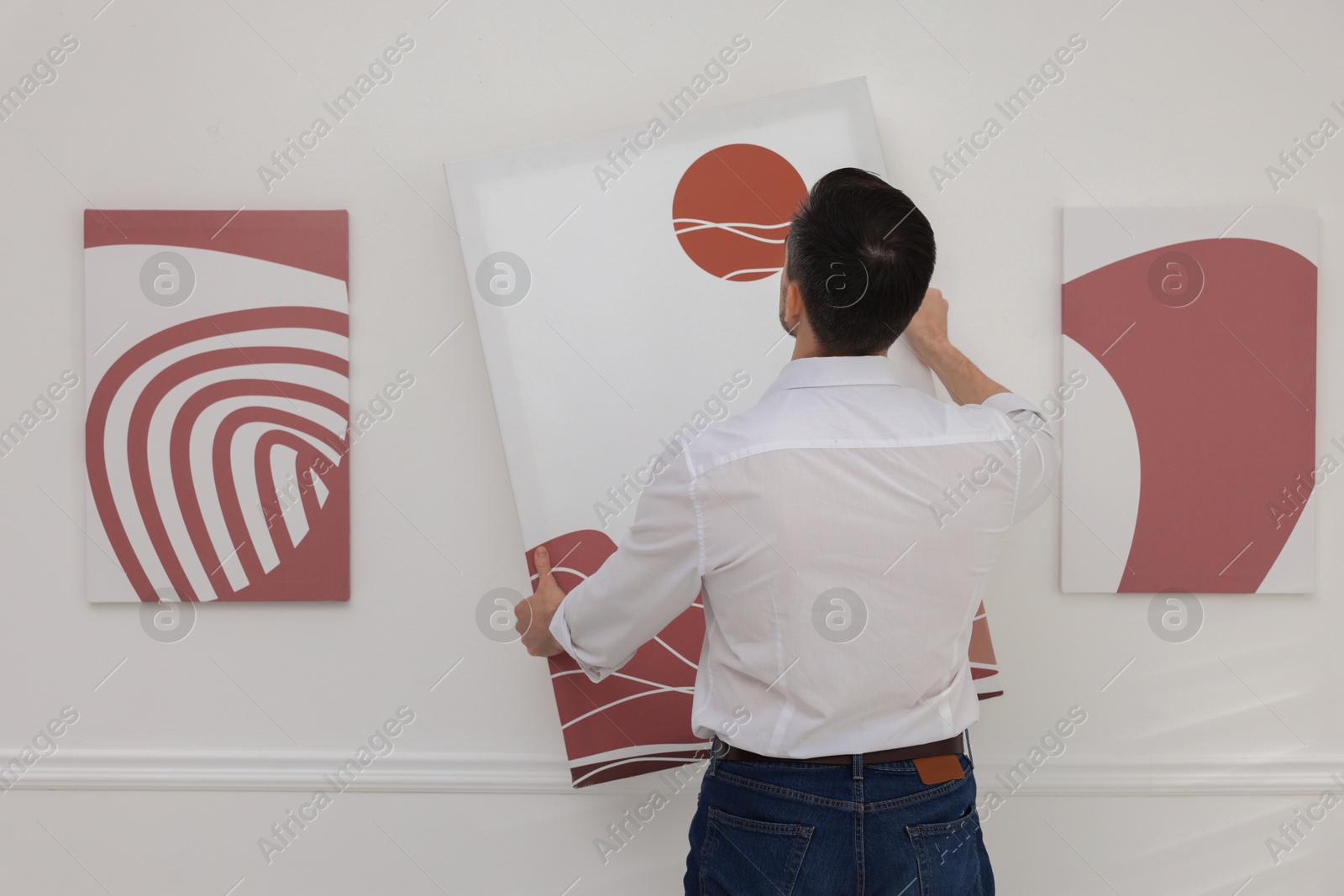 Photo of Man hanging painting on wall in art gallery, back view