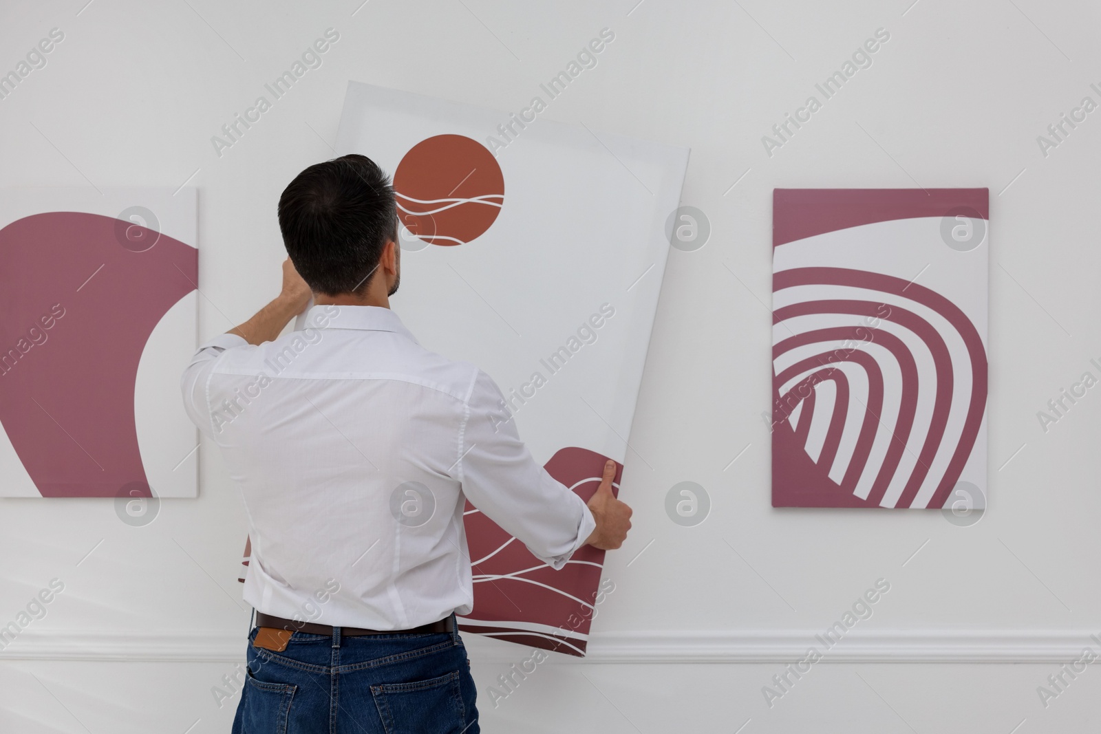 Photo of Man hanging painting on wall in art gallery, back view