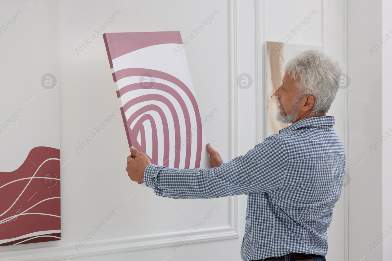 Photo of Man hanging painting on wall in art gallery