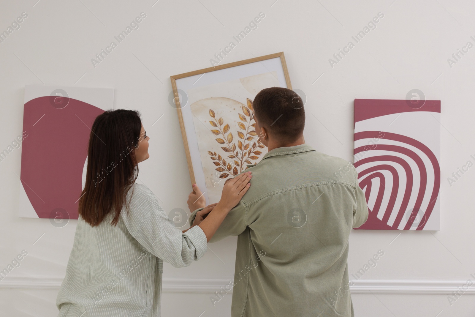 Photo of Man and woman hanging paintings on wall in art gallery, back view