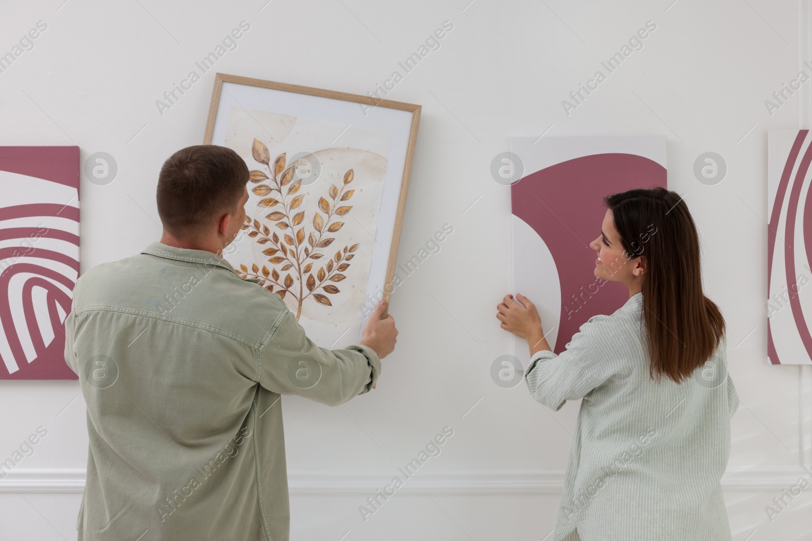 Photo of Man and woman hanging paintings on wall in art gallery, back view