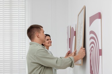 Photo of Man and woman hanging paintings on wall in art gallery