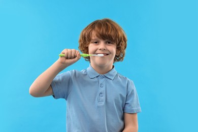 Photo of Cute boy brushing his teeth on light blue background