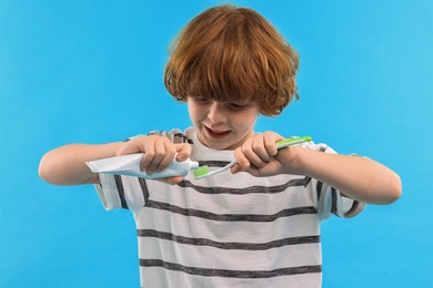 Photo of Cute boy applying paste on toothbrush against light blue background