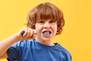 Photo of Cute boy brushing his teeth on yellow background