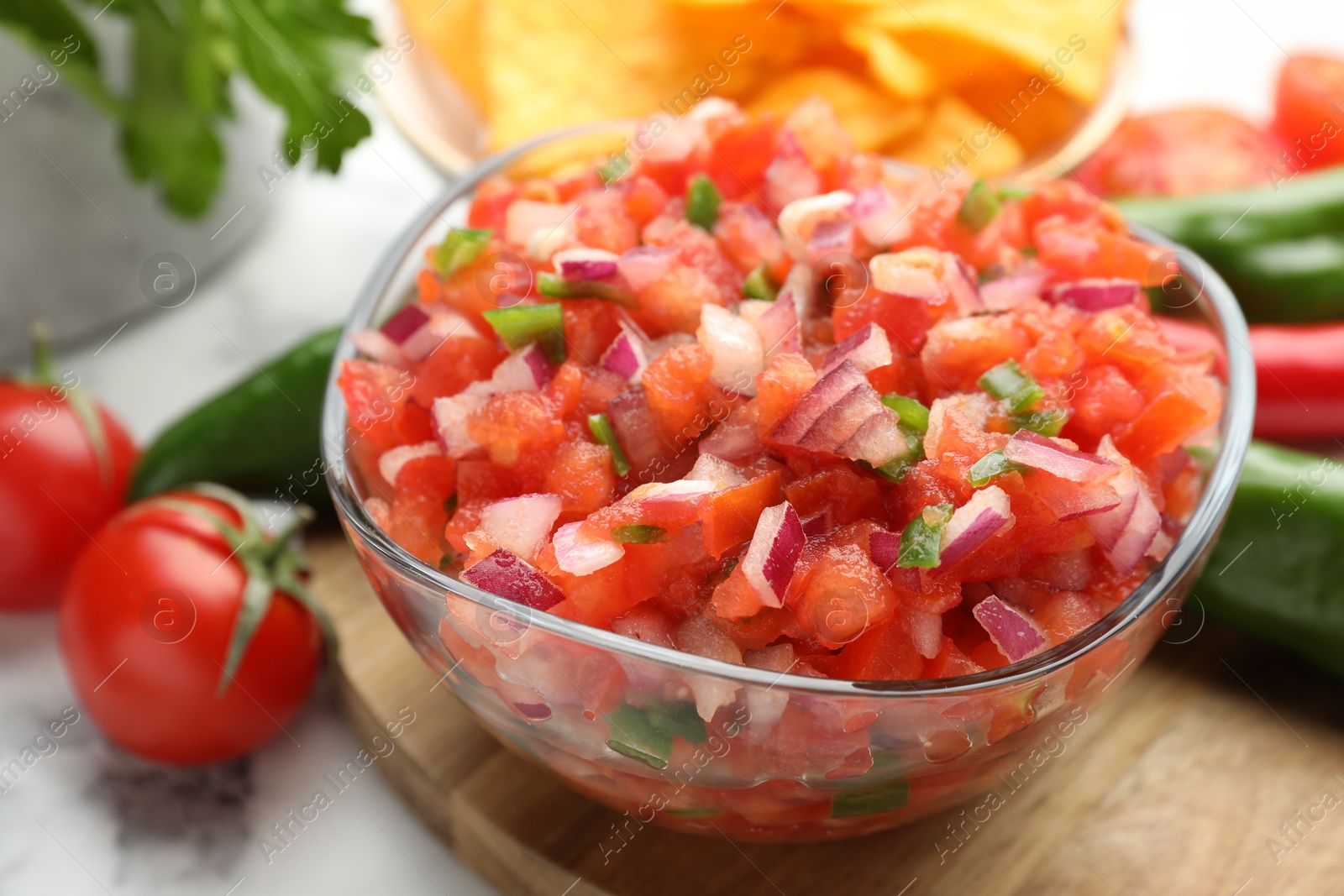 Photo of Delicious salsa in glass bowl and ingredients on white table, closeup