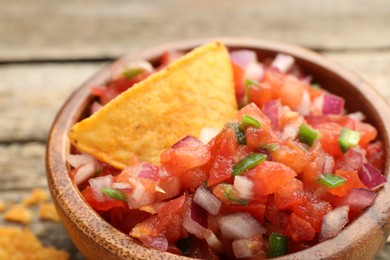 Delicious salsa and nacho chip in bowl on table, closeup