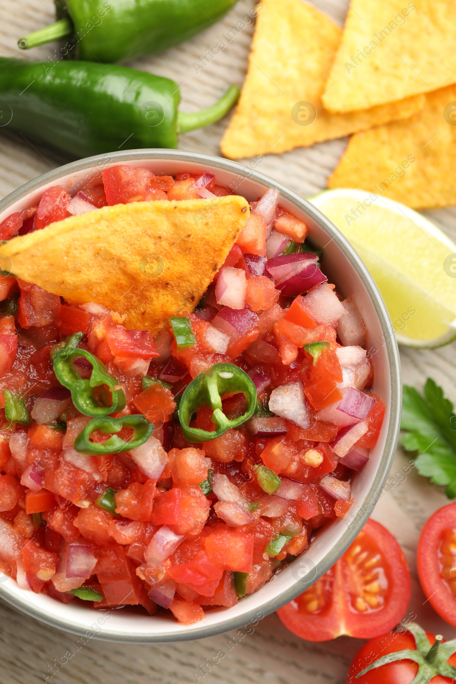 Photo of Delicious salsa in bowl, nacho chips and ingredients on wooden table, flat lay