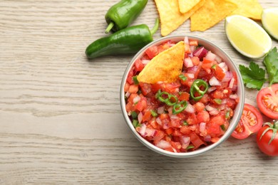 Delicious salsa in bowl, nacho chips and ingredients on wooden table, flat lay. Space for text