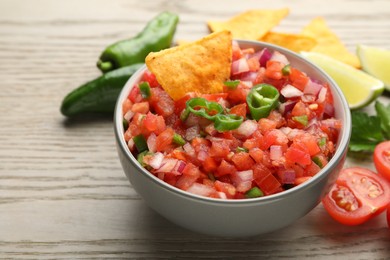 Delicious salsa and nacho chip in bowl on wooden table, closeup