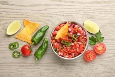 Delicious salsa in bowl, nacho chips and ingredients on wooden table, flat lay