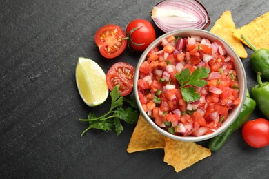 Delicious salsa in bowl, nacho chips and ingredients on grey table, flat lay. Space for text