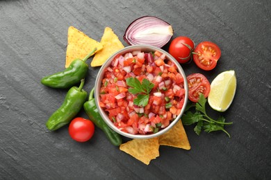 Delicious salsa in bowl, nacho chips and ingredients on grey table, flat lay