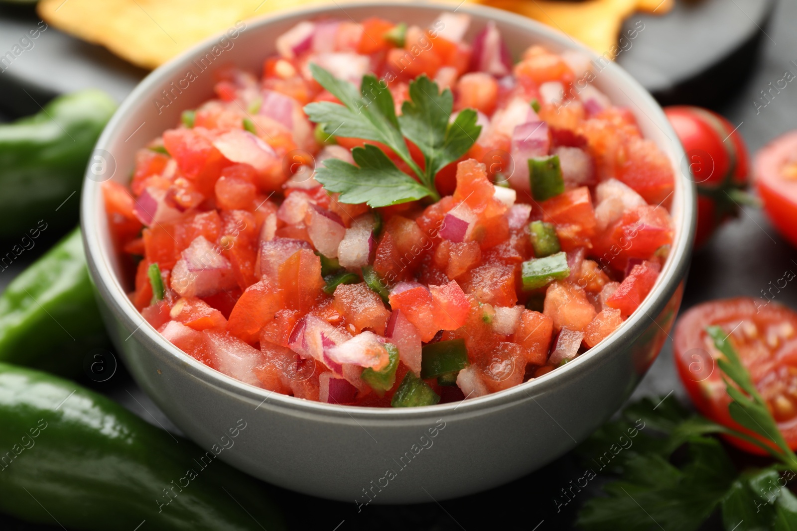 Photo of Delicious salsa in bowl and ingredients on grey table, closeup