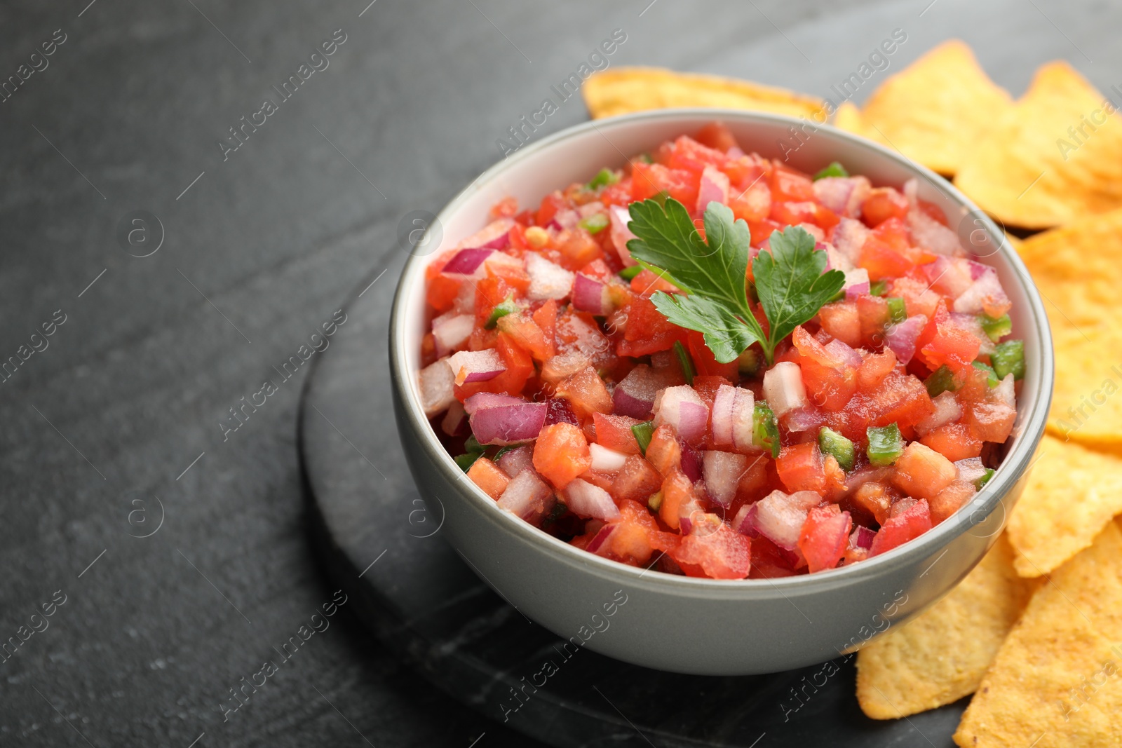 Photo of Delicious salsa in bowl and nacho chips on grey table, closeup. Space for text