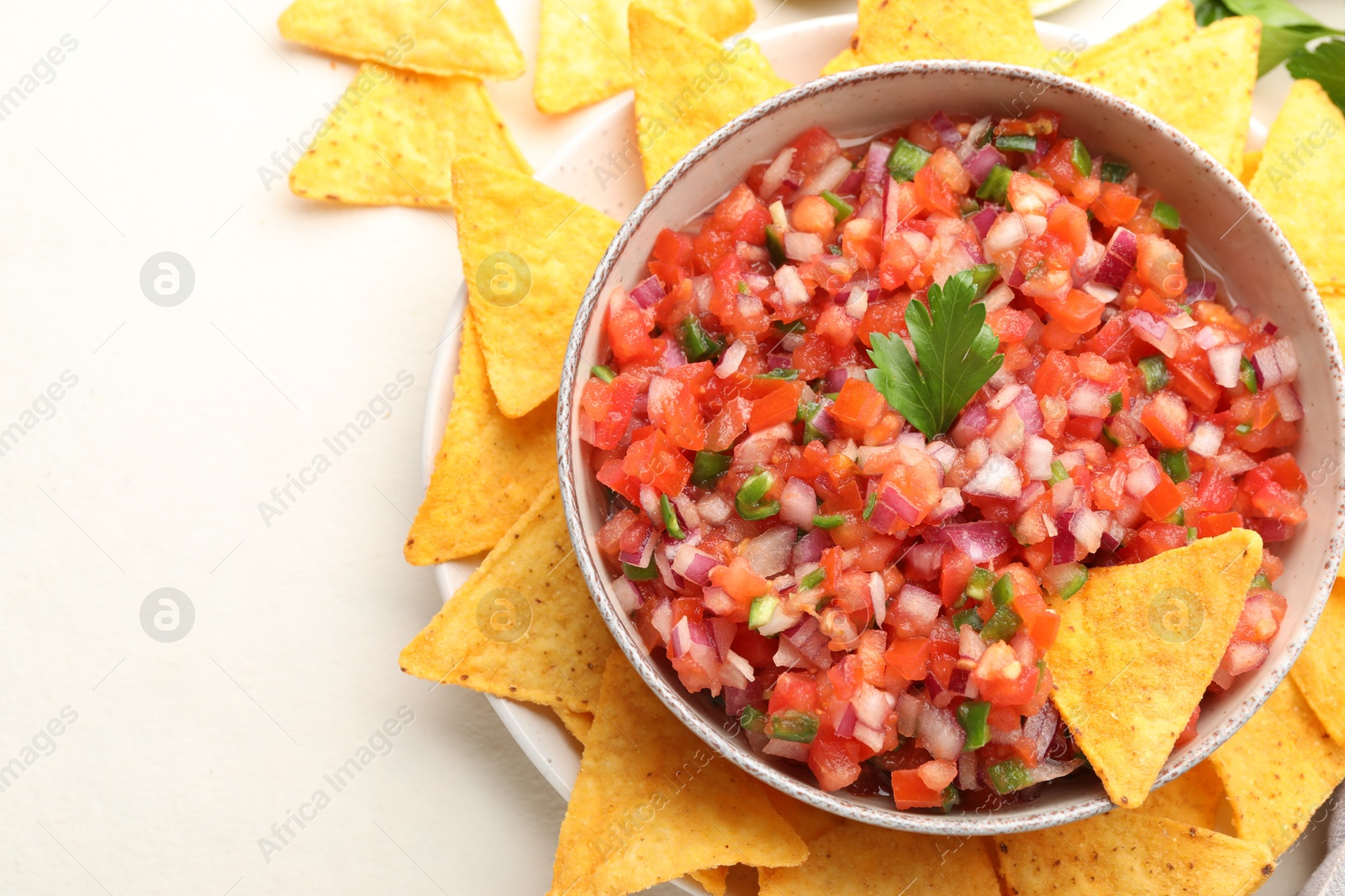 Photo of Delicious salsa in bowl and nacho chips on light table, flat lay. Space for text