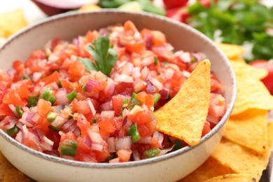 Delicious salsa in bowl and nacho chips on table, closeup