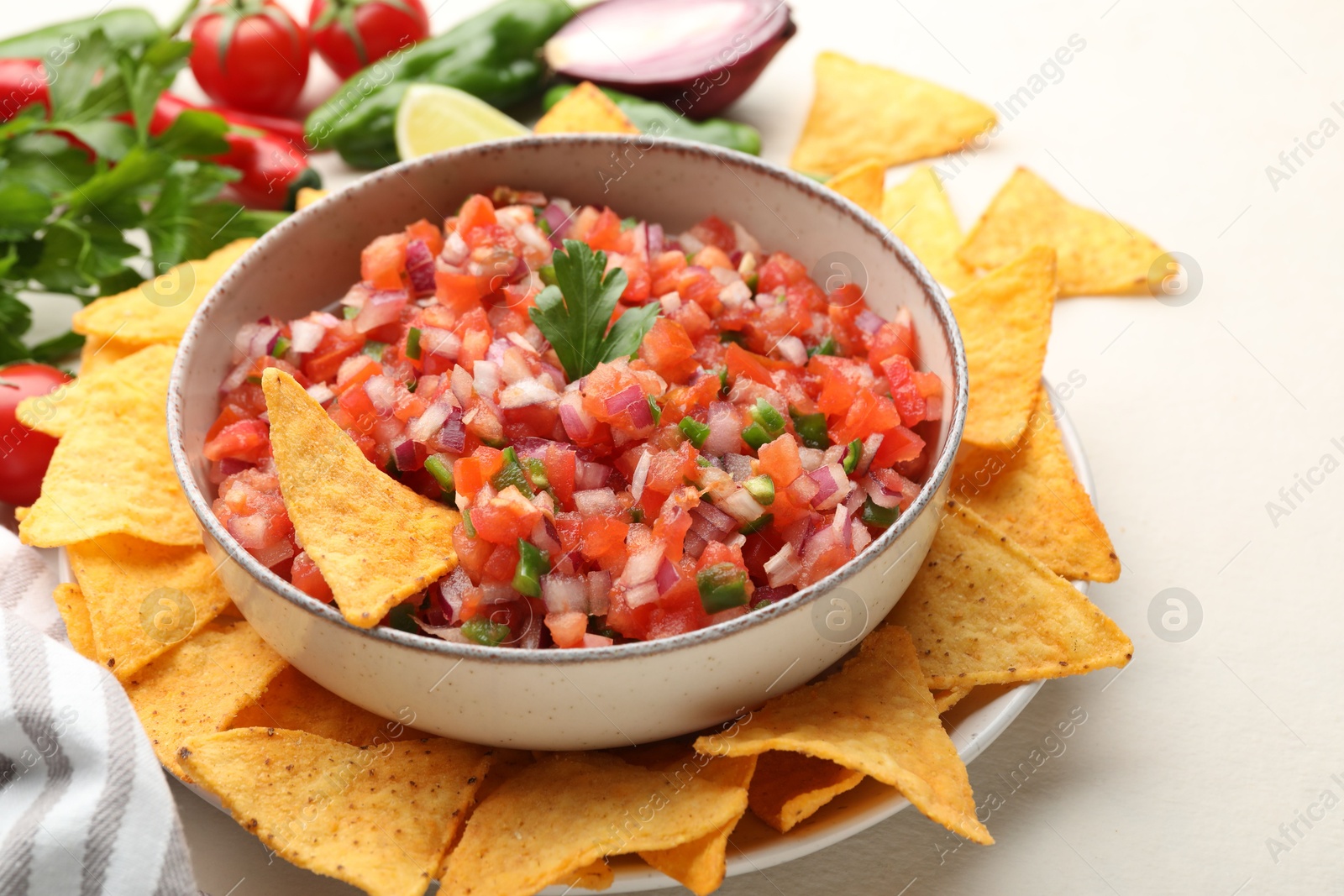 Photo of Delicious salsa in bowl, ingredients and nacho chips on light table