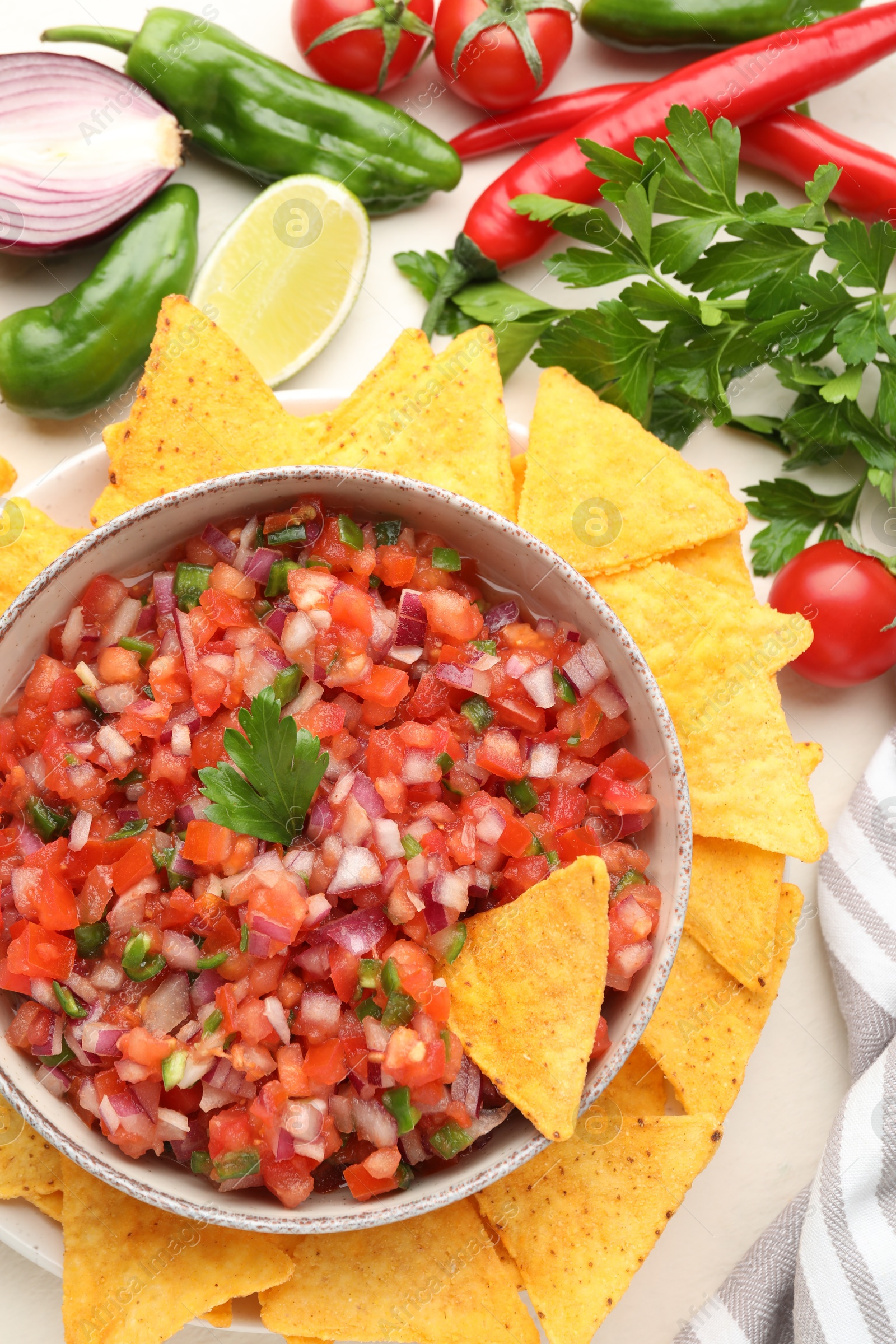 Photo of Delicious salsa in bowl, ingredients and nacho chips on beige table, flat lay