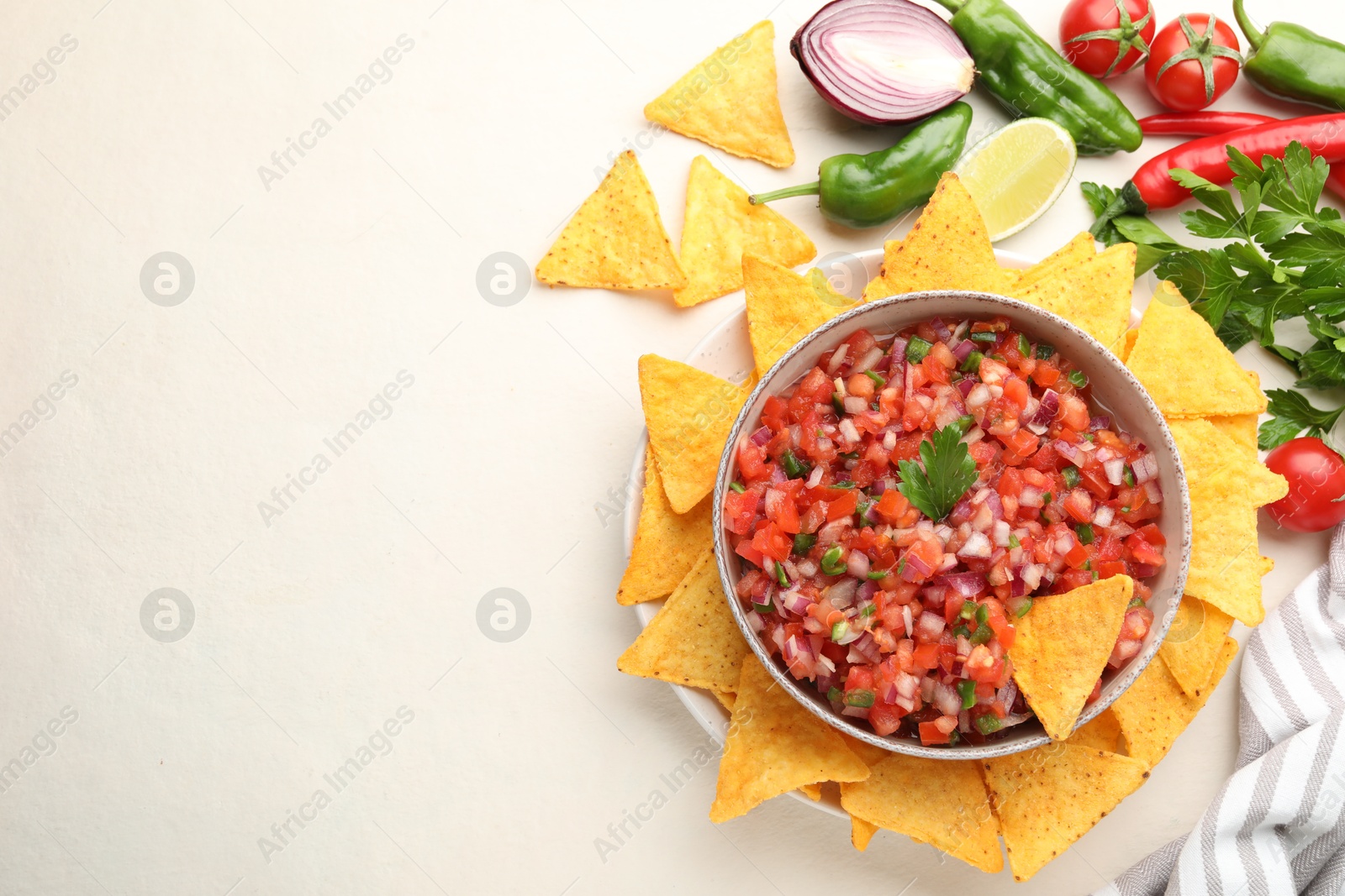 Photo of Delicious salsa in bowl, ingredients and nacho chips on beige table, flat lay. Space for text