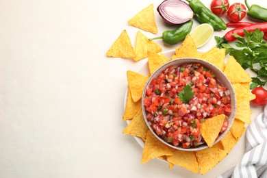 Delicious salsa in bowl, ingredients and nacho chips on beige table, flat lay. Space for text