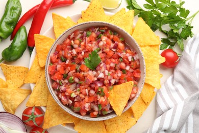 Delicious salsa in bowl, ingredients and nacho chips on beige table, flat lay