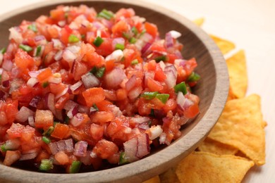 Delicious salsa in bowl and nacho chips on table, closeup