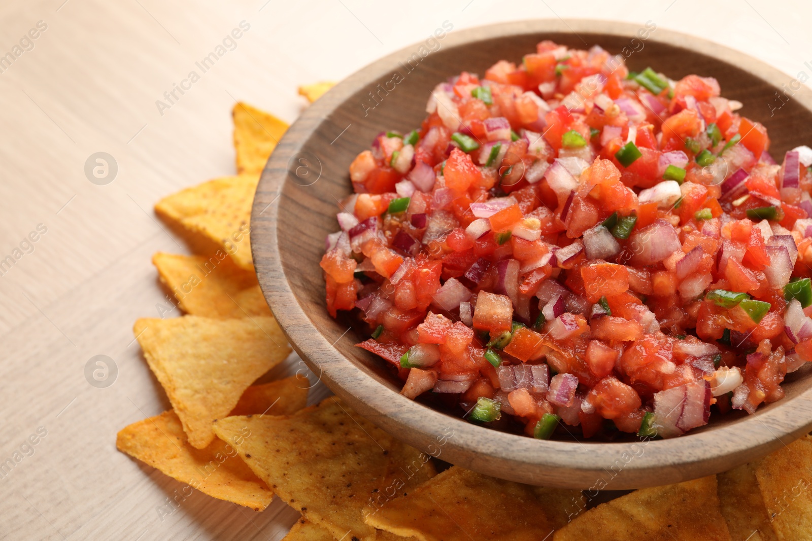 Photo of Delicious salsa in bowl and nacho chips on wooden table, closeup