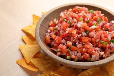 Delicious salsa in bowl and nacho chips on wooden table, closeup