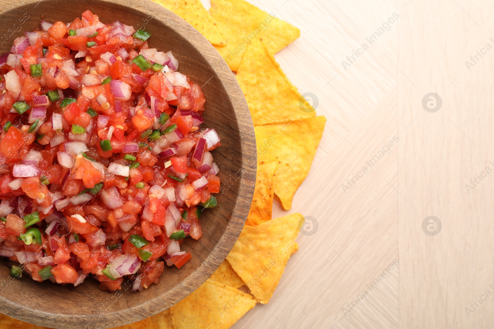 Photo of Delicious salsa in bowl and nacho chips on wooden table, top view. Space for text