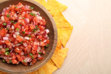 Delicious salsa in bowl and nacho chips on wooden table, top view. Space for text