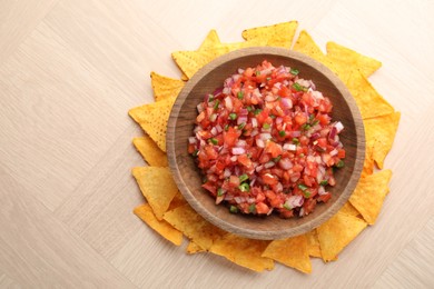 Delicious salsa in bowl and nacho chips on wooden table, top view. Space for text