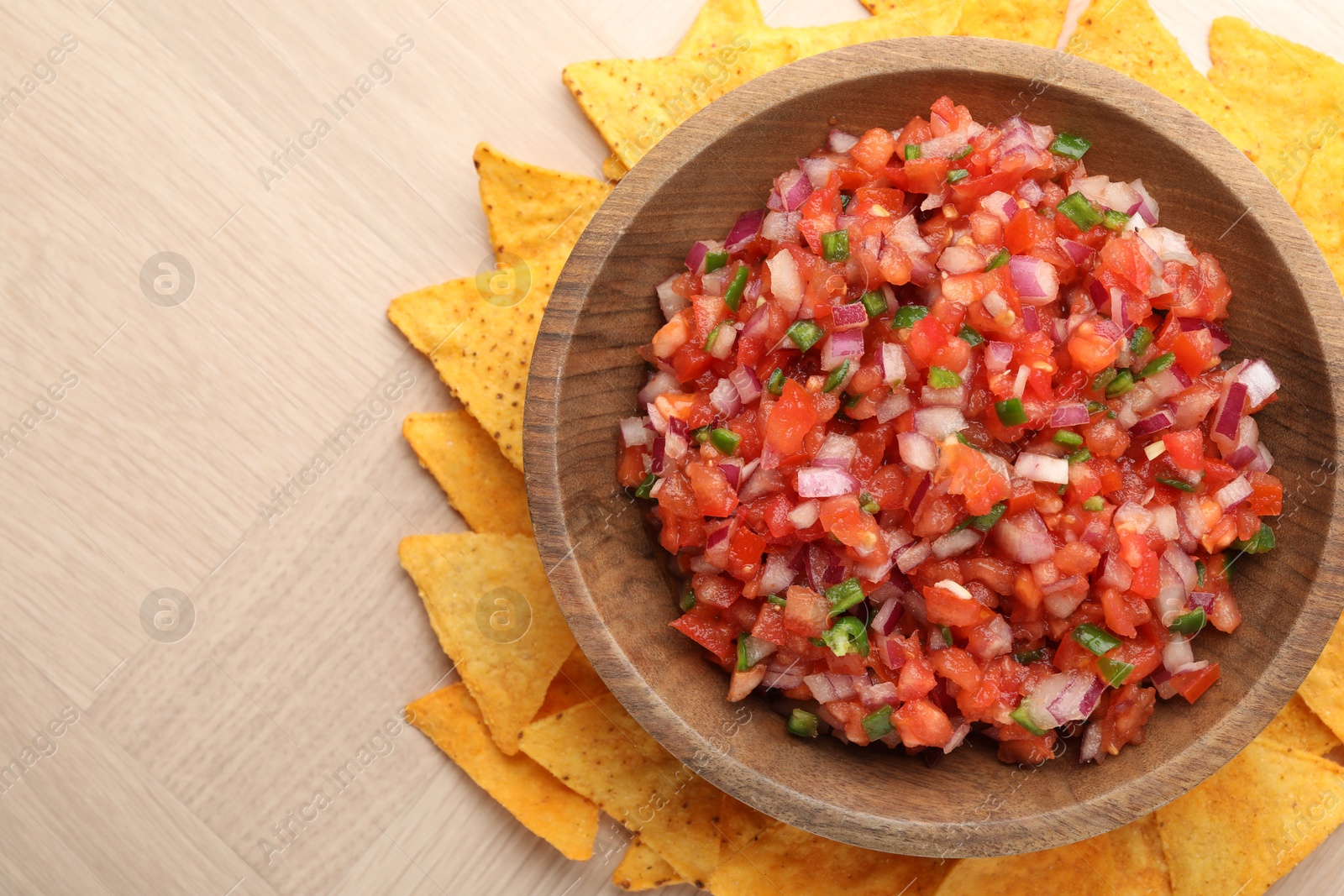 Photo of Delicious salsa in bowl and nacho chips on wooden table, top view. Space for text