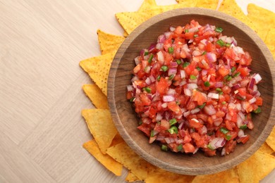 Delicious salsa in bowl and nacho chips on wooden table, top view. Space for text