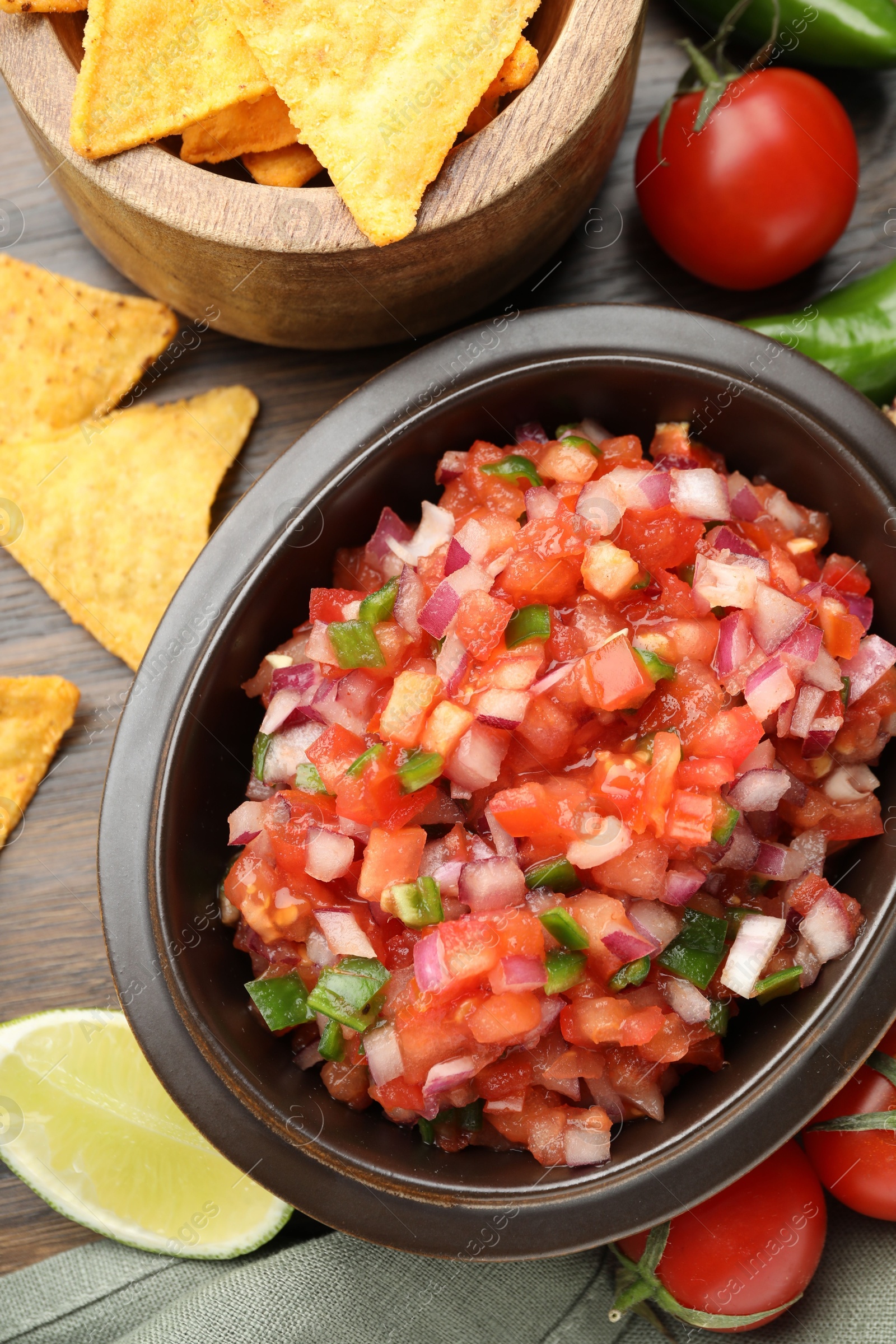 Photo of Delicious salsa in bowl, nacho chips and ingredients on wooden table, flat lay