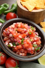 Photo of Delicious salsa in bowl, nacho chips and ingredients on table, closeup