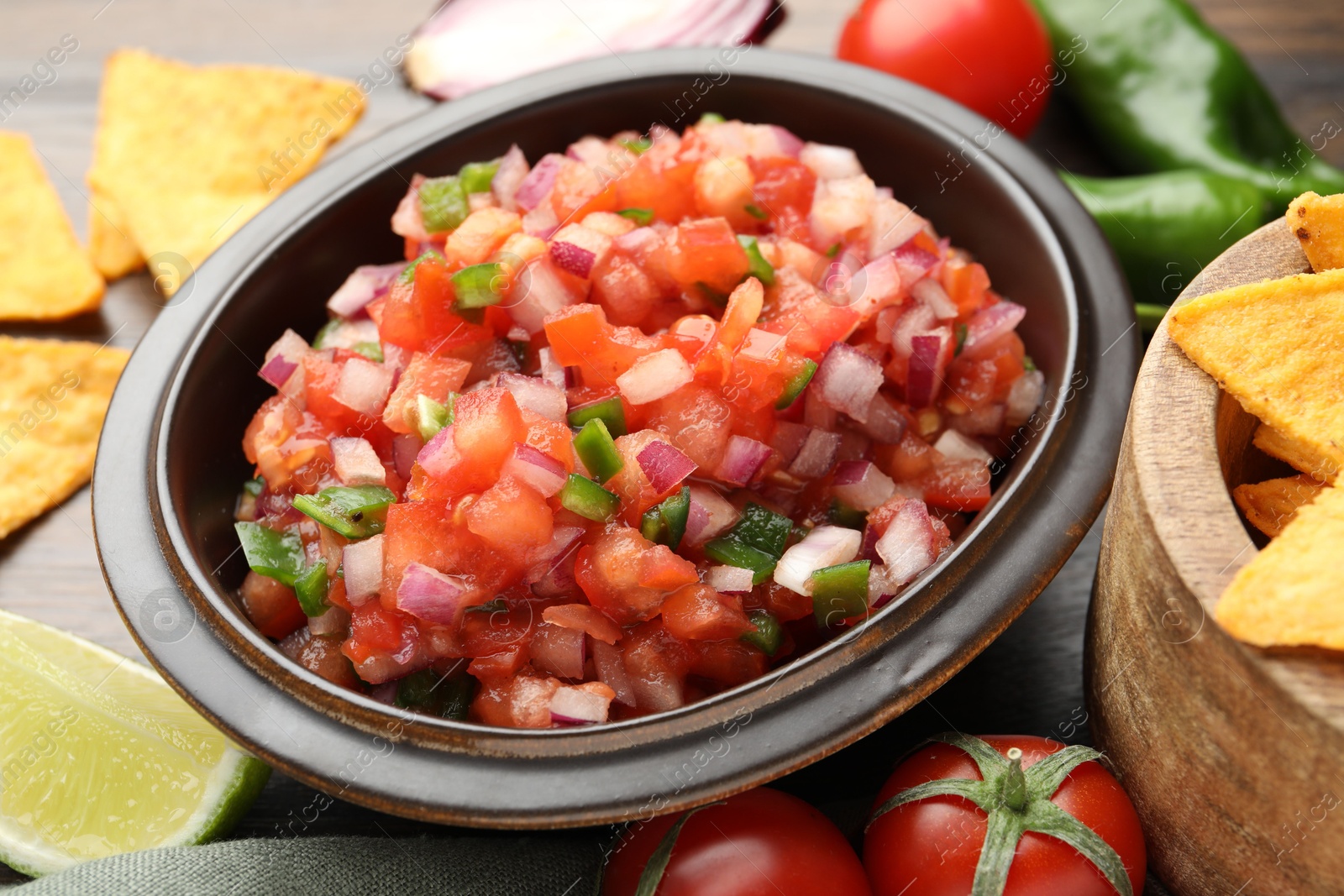 Photo of Delicious salsa in bowl, nacho chips and ingredients on table, closeup