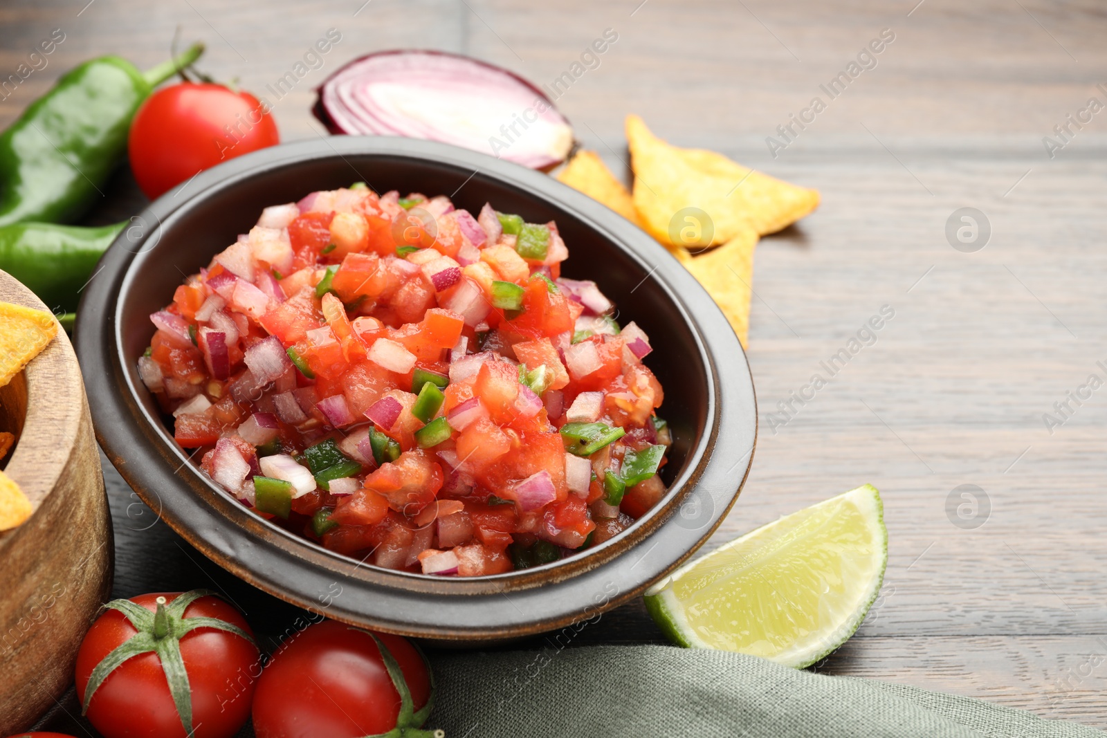 Photo of Delicious salsa in bowl, nacho chips and ingredients on wooden table, closeup. Space for text