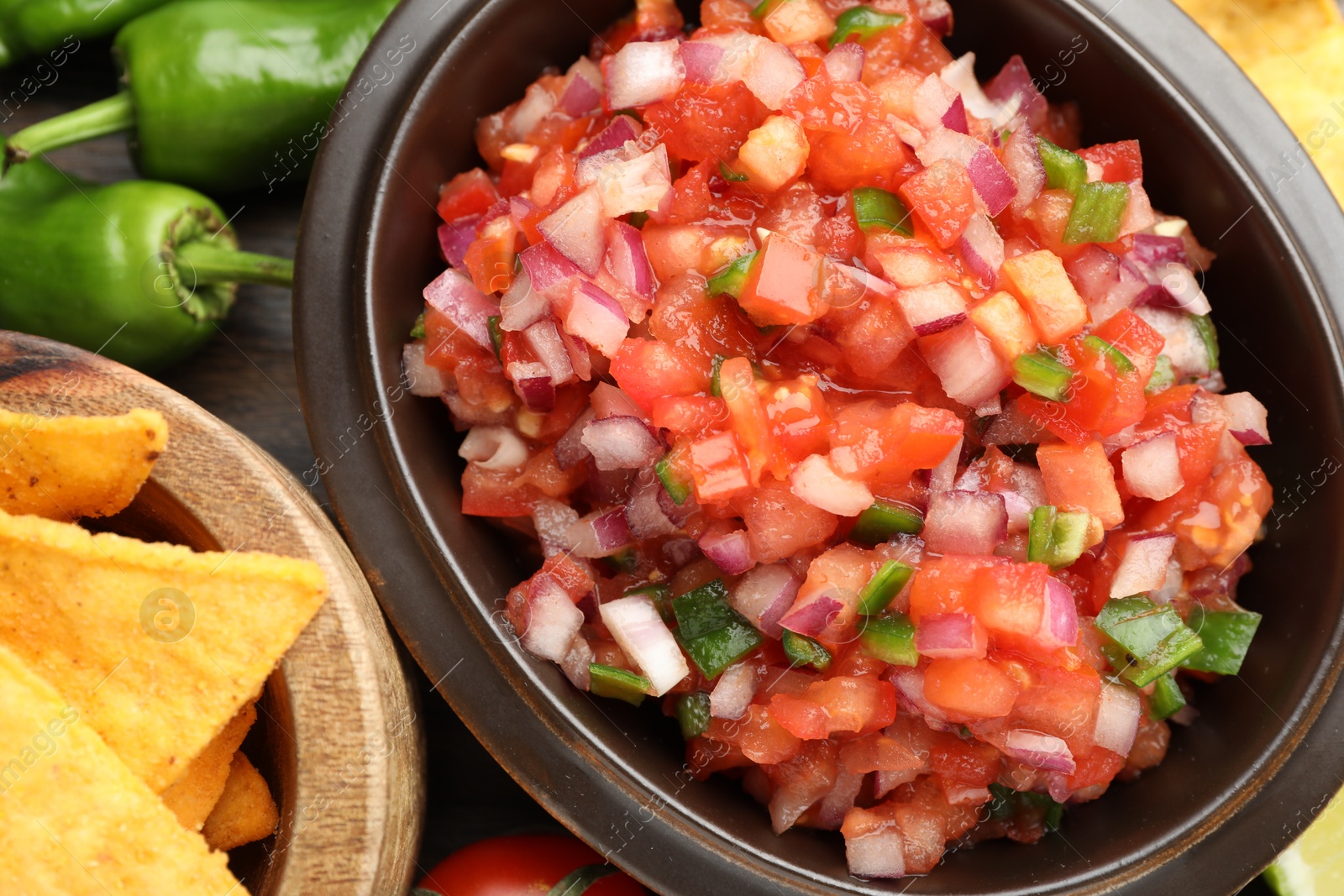 Photo of Delicious salsa in bowl, nacho chips and ingredients on table, closeup