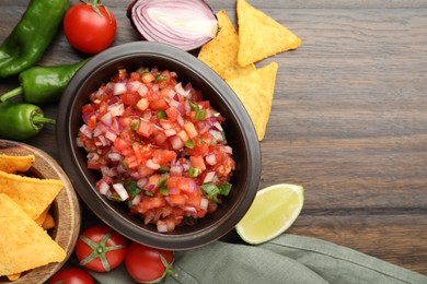 Delicious salsa in bowl, nacho chips and ingredients on wooden table, flat lay. Space for text